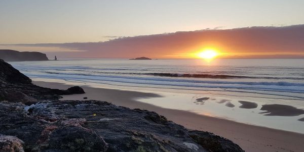 The sun sets over the Atlantic surf rolling in to Sandwood beach