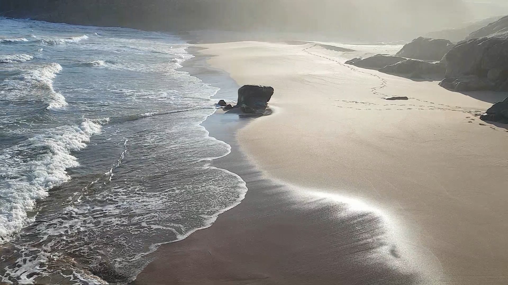 Early morning sun and mist light up the sand as a small surf hits the beach near Sandwood, Scotland