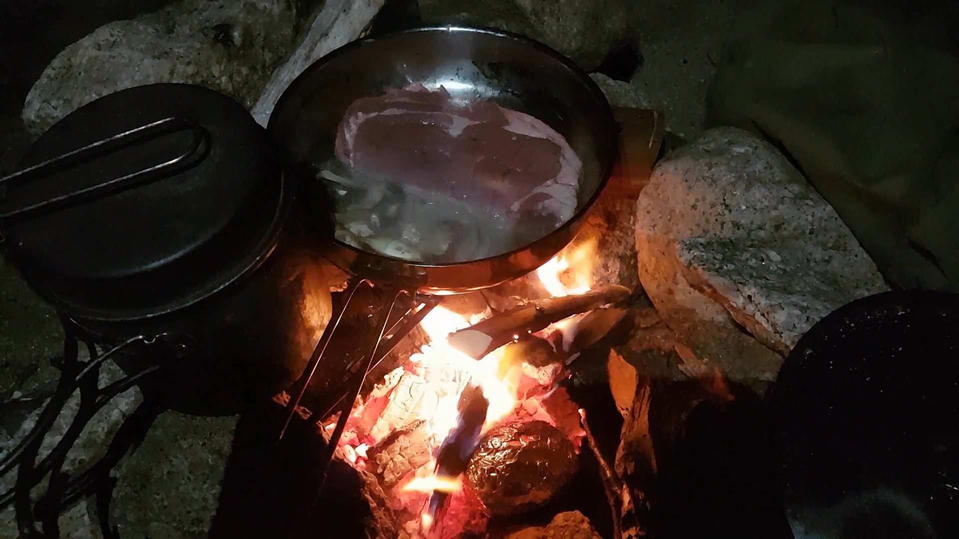 Steak and mushrooms cook over an open fire as night falls